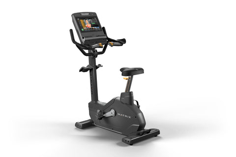 Matrix Endurance upright exercise bike with black frame, digital display console, dual handles, and black padded seat on whit