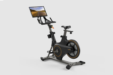 Black stationary exercise bike with orange accents, tablet console mounted on handlebar displaying road scenery, on white bac