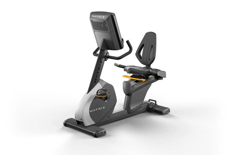 Black and gray Matrix recumbent exercise bike with digital display screen, padded seat, and foot pedals on white background