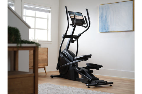 Black elliptical machine with curved handles, digital display console, and moving foot pedals on white background