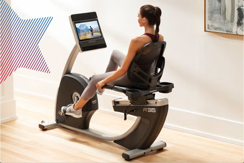 Black and silver recumbent exercise bike with mesh backrest, digital display monitor, and attached tablet holder on white bac