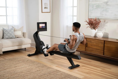 Black NordicTrack RW700 rowing machine with digital display monitor showing fitness video, featuring extended seat rail and f