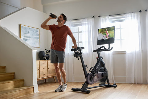 Black NordicTrack stationary bike with curved handlebars, seat, and pedals, topped with mounted tablet display showing cyclin