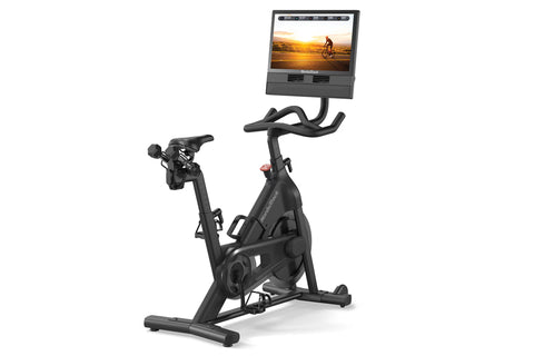 Black NordicTrack stationary bike with curved handlebars, seat, and pedals, topped with mounted tablet display showing cyclin