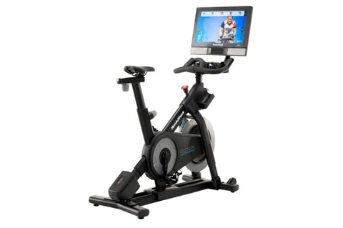 Black indoor stationary exercise bike with touchscreen display console mounted on adjustable arm, shown on white background