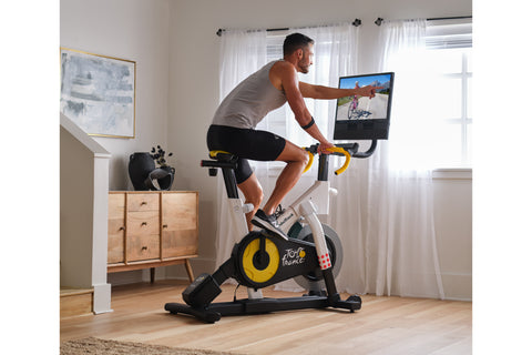 NordicTrack Tour de France indoor stationary bike with white frame, yellow and black flywheel, yellow handlebars, and attache