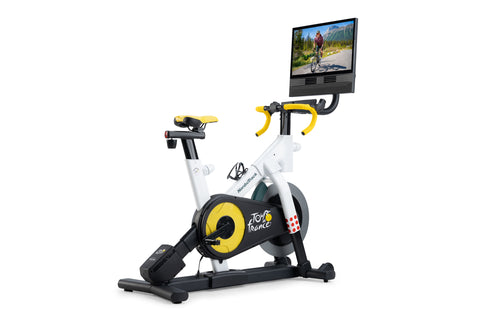 NordicTrack Tour de France indoor stationary bike with white frame, yellow and black flywheel, yellow handlebars, and attache