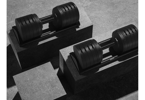 Pair of NuoBell adjustable dumbbells with black rubber-coated plates and silver handle, shown stacked on white background