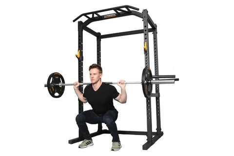 Black power rack with integrated pull-up bar and safety arms, shown with male model demonstrating squat position with loaded 