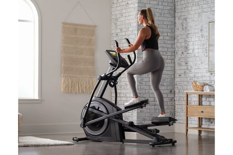Woman using black ProForm Plus Carbon E7 elliptical machine with digital display in home gym setting
