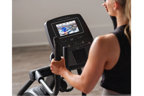 Woman using black ProForm Plus Carbon E7 elliptical machine with digital display in home gym setting
