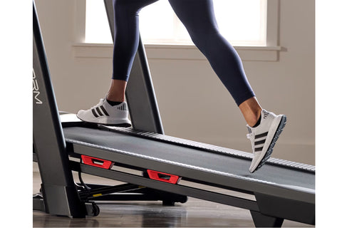 Woman running on black ProForm Plus Trainer 1000 treadmill with digital display in modern home gym setting