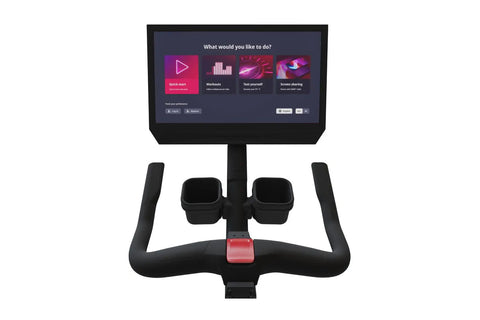 Black stationary exercise bike with digital touchscreen display mounted on upper frame, padded seat, handlebars, and foot ped
