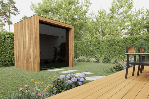 Modern wooden cube sauna with dark interior and windows, situated on composite deck surrounded by landscaping and garden furn