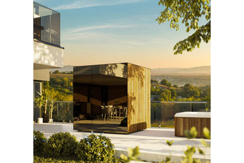 Modern outdoor sauna with natural wood and charcoal exterior in garden setting with hedges and flowering plants