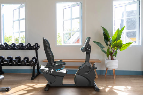 Black recumbent exercise bike with mesh backrest, digital display console, and foot pedals on white background