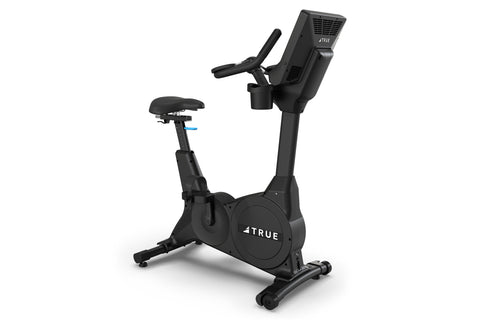 Black upright exercise bike with digital display console, padded seat, and handlebars on white background