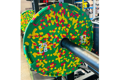 Colorful bumper plates with speckled rubber coating displayed on gym floor, including gray with red flecks, yellow with red f