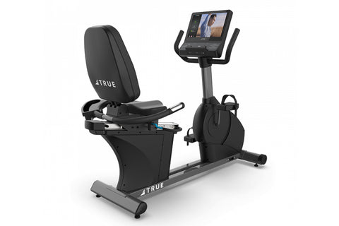 TRUE CS400 commercial recumbent stationary bike with black seat and frame, digital display console, and foot pedals on white 