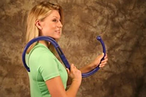 Woman wearing green t-shirt holding blue S-shaped massage tool behind her back against textured brown background
