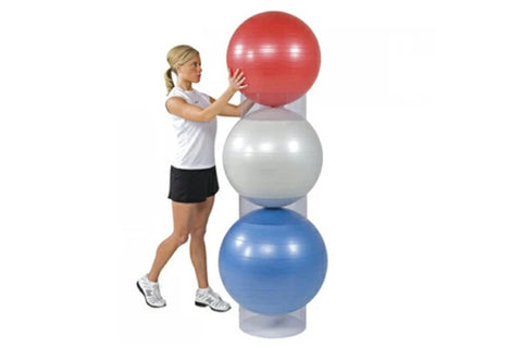 Woman in white tank top and black shorts holding red stability ball stacked on silver and blue exercise balls with gray rings