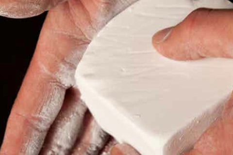 Hand holding white chalk block against skin, demonstrating product texture and grip