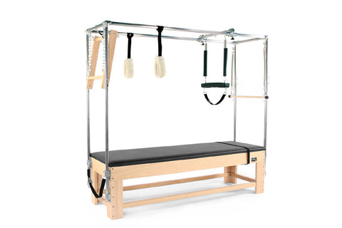 Pilates reformer with wood base, black padded bed, metal frame, and attached accessories including footbar, straps, and woode
