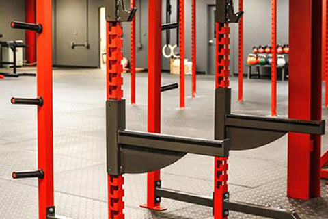 Commercial power cage with red steel frame and black safety bars in gym setting with equipment visible in background