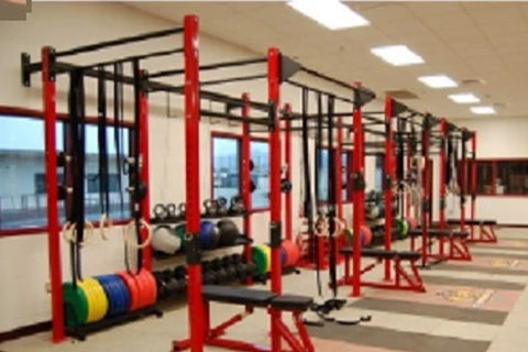 Red and black commercial workout rig with pull-up bars, heavy bag stations, and weight plates in gym setting