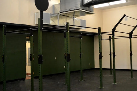 Green and black steel pull-up bar rig with multiple stations in gym setting