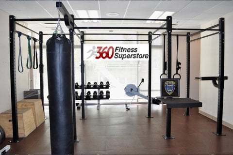 Black steel cage training rig with heavy bag and pull-up bars in gym setting