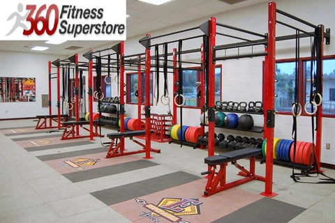 Red and black commercial gym rig system with pull-up bars, weight plates, kettlebells, and exercise balls in fitness facility