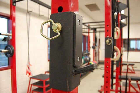Black padded J-hook attachment with brass ring, mounted on red gym rack equipment