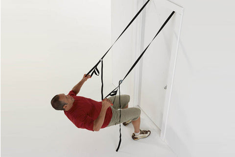 Man using black suspension training straps mounted in doorway, wearing red shirt and khaki shorts, demonstrating upper body e