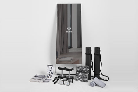 Lululemon Studio Mirror with black carrying cases, yoga mats, water bottle, towels, and accessories displayed on white backgr