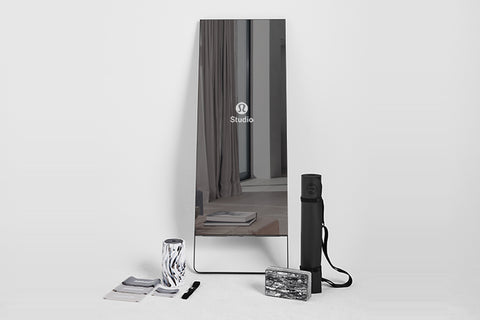 Lululemon Studio Mirror Plus with black frame standing upright, displaying studio reflection, surrounded by accessories inclu