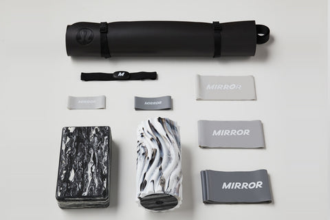 Lululemon Studio Mirror Plus with black frame standing upright, displaying studio reflection, surrounded by accessories inclu