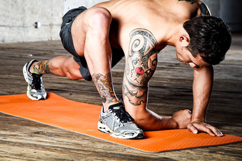 Man performing plank exercise on orange Natural Fitness PowerHouse Promat, wearing black shorts and white sneakers