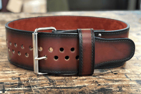 Black leather power belt with blue interior, metal buckle, and double-row metal grommets, flat lay on wooden surface