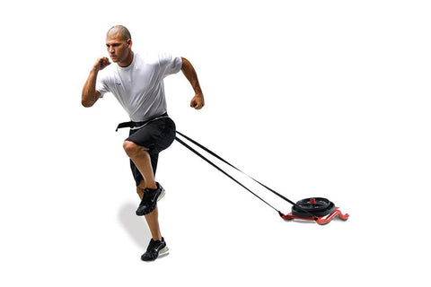 Man wearing white t-shirt and black shorts using black and red power sled with waist belt harness on white background