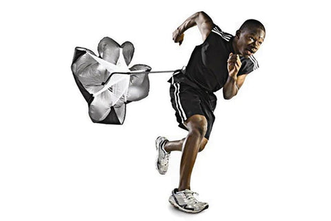 Man wearing black athletic shorts with white stripes and white sneakers running with resistance parachute chute on white back