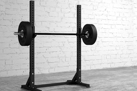 Black power squat stand with adjustable height uprights and loaded barbell, displayed against white brick wall