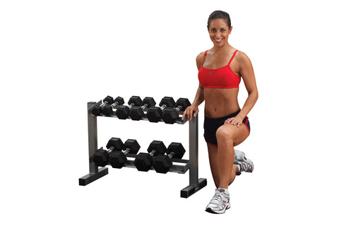 Woman in red sports bra and black shorts posing next to two-tier dumbbell rack with black hex dumbbells on white background