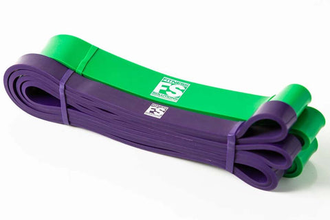 Purple and green resistance loop bands rolled and stacked with green handles on white background