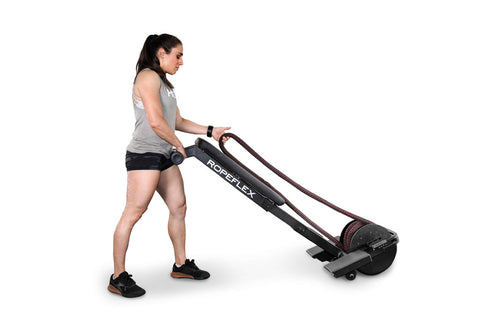 Man wearing red Ropeflex t-shirt and black shorts using black Ropeflex RX2200 horizontal rope trainer on white background