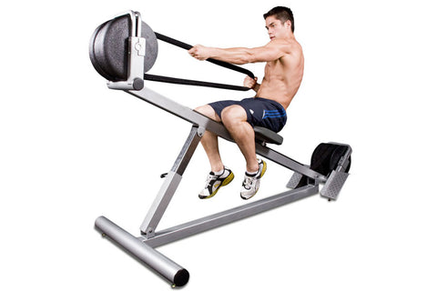 Shirtless man using gray and black incline rope trainer with medicine ball attachment, demonstrating exercise form against wh