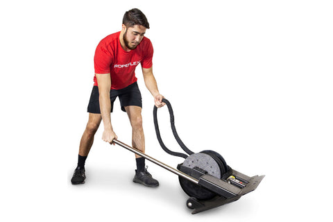 Man in red shirt and black shorts using black Ropeflex rope trainer while seated on exercise ball