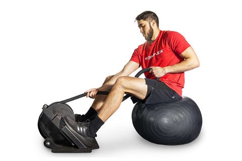 Man in red shirt and black shorts using black Ropeflex rope trainer while seated on exercise ball