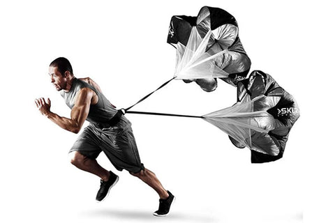 Man running in gray tank top and black shorts using black and white speed training parachute for resistance
