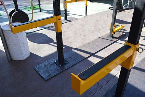 Yellow and black safety bar attachment with foot platform, mounted on outdoor fitness equipment frame